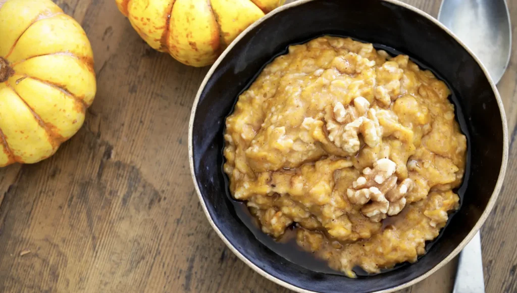 pumpkin oatmeal in a bowl with small yellow pumpkins in the left hand side