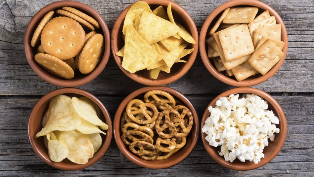 6 containers filled with snacks: crackers, chips, pretzels and popcorn 