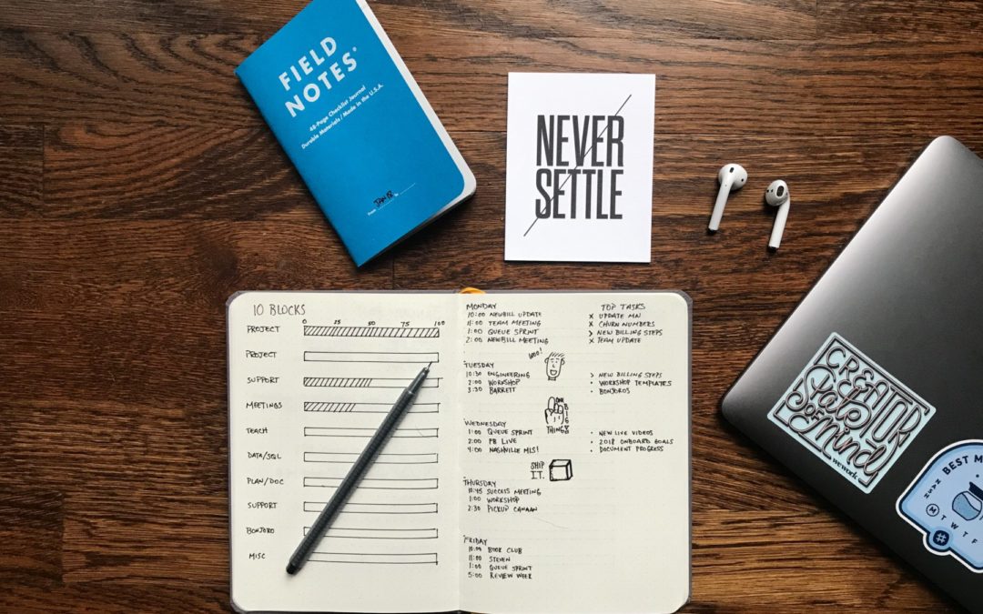 notebook with pen, piece of paper that says "never settle" on a wood desk