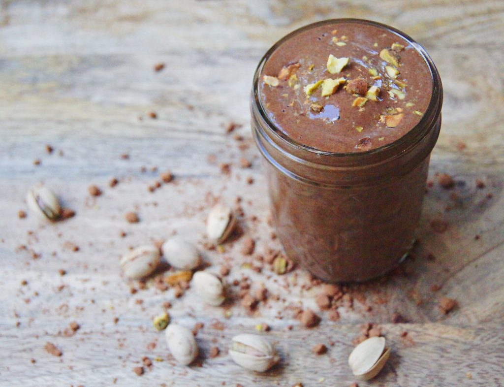 chocolate smoothie with pistachio nuts and cocoa powder on a wood table