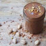 chocolate smoothie with pistachio nuts and cocoa powder on a wood table