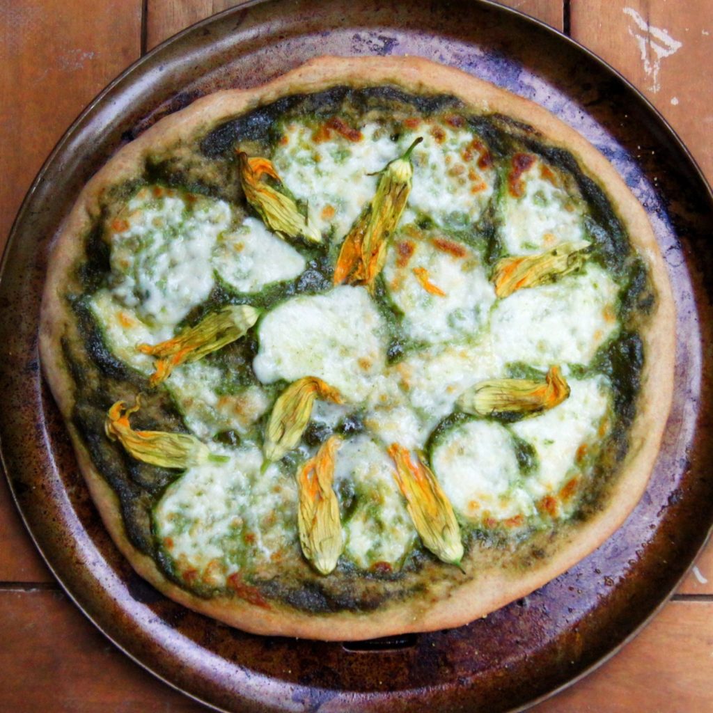 a whole squash blossom pizza with basil sauce on a pizza pan