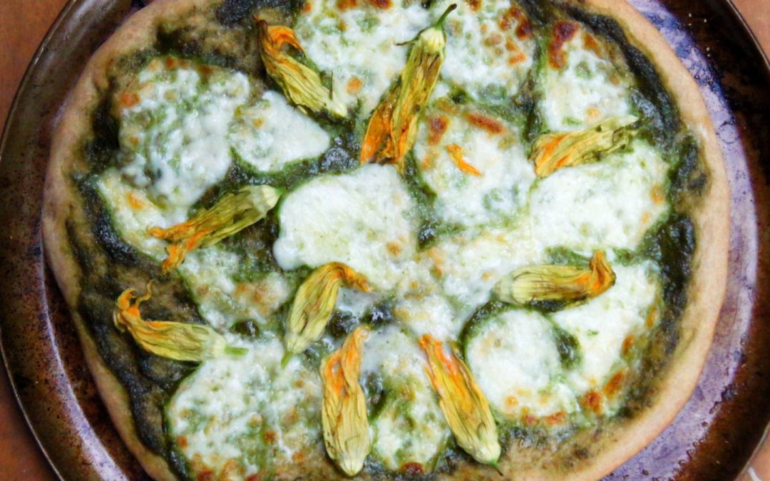 a whole squash blossom pizza with basil sauce on a pizza pan
