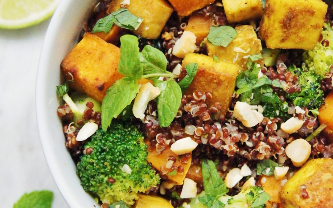 Curry, quinoa, tofu, sweet potatoes in a bowl with cashews, mint and yogurt sauce on the side.