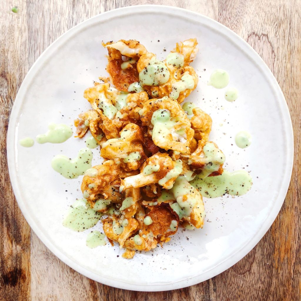 baked and breaded cauliflower bites on a white plate with avocado sauce dressing