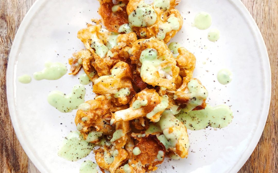 baked and breaded cauliflower bites on a white plate with avocado sauce dressing