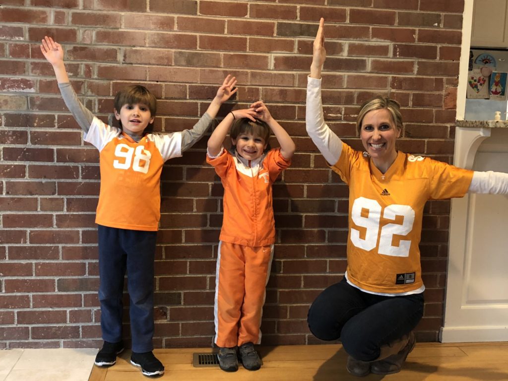 mom and two sons dressed in tennessee volunteer jerseys spelling V O L S with their arms