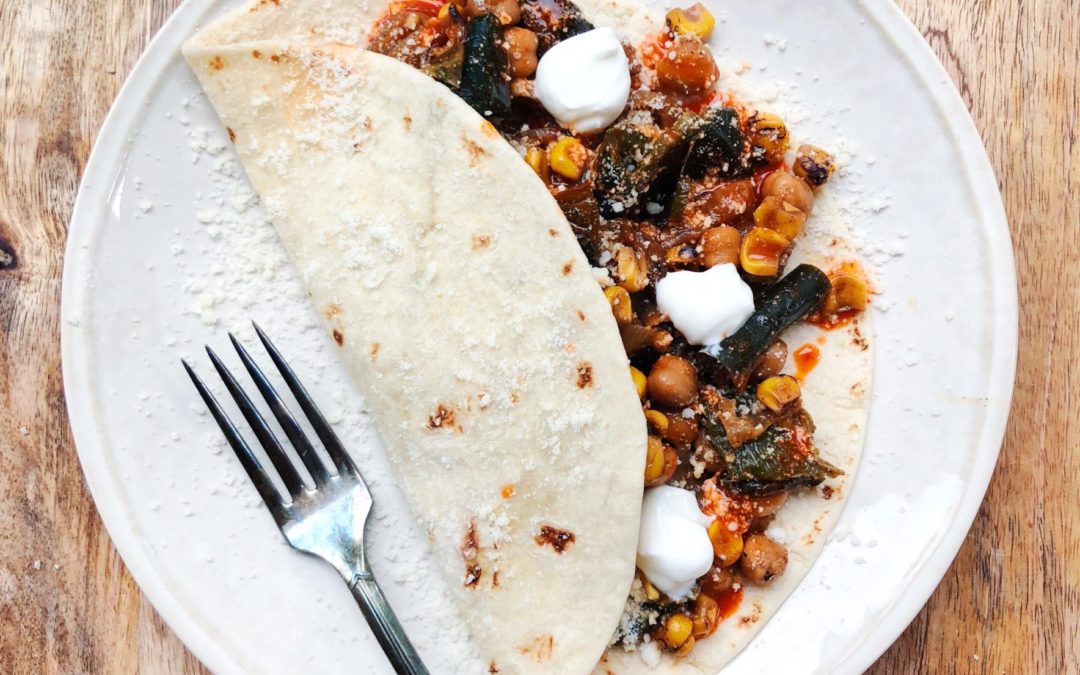 Soft taco on a plate with a fork filled with veggies and topped with cheese and greek yogurt