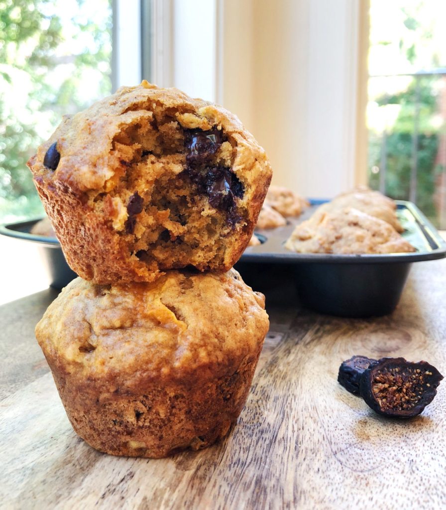 two sweet potato muffins stacked on top of each other, one has a bite out of it, and you can see the chocolate chips inside