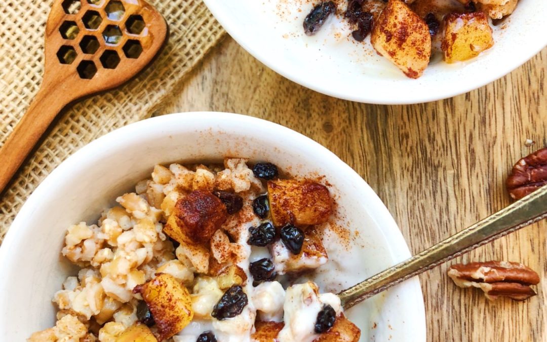 farro breakfast bowl with apples, cinnamon, pecans and currants, honey stick is laying beside the bowl