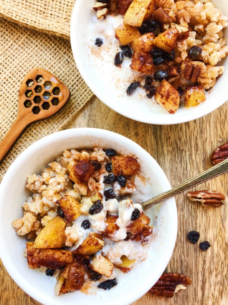 farro breakfast bowl with apples, cinnamon, pecans and currants, honey stick is laying beside the bowl