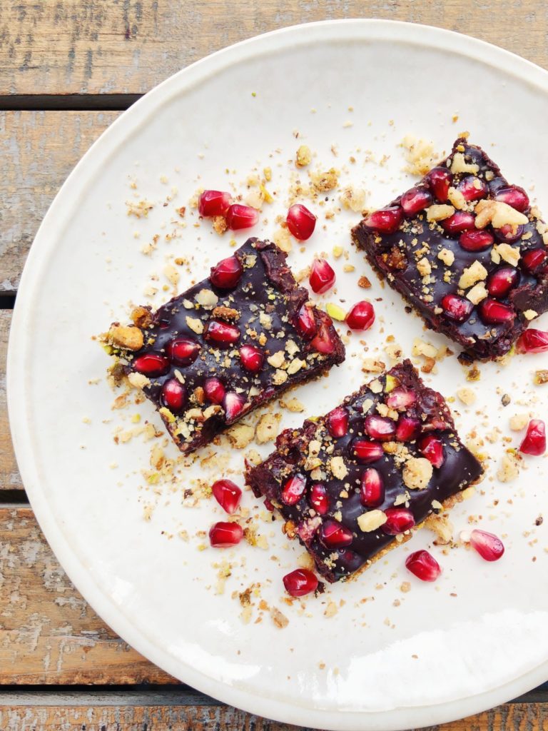 no bake chocolate pomegranate squares, 3 squares on a plate, sprinkled with nuts and pomegranate seeds