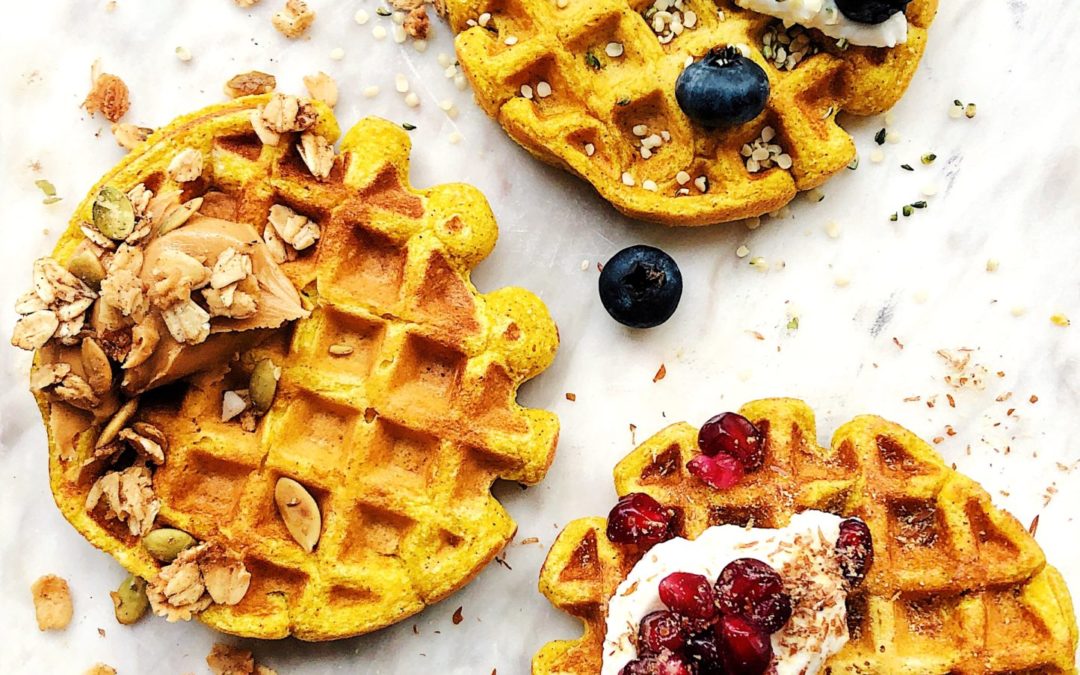 3 waffles with topped with blueberries, pomegranate seeds, nut butter and greek yogurt + hemp and flax seeds on a white cutting board