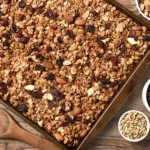 overhead shot of granola on a baking sheet with almonds and cherries