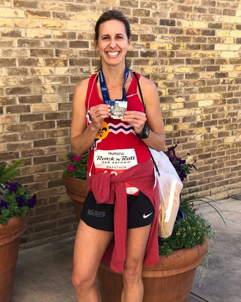marathoner wearing her medal in front of a brick building