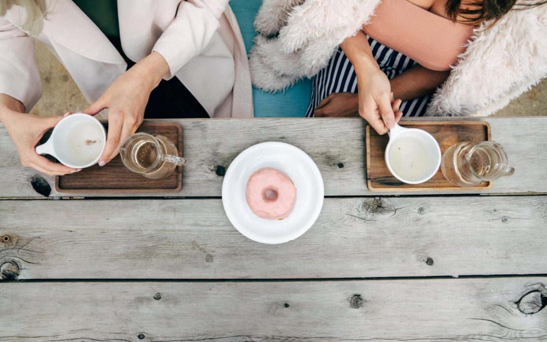 overhead shot of two women drinking tea and have a donut in the middle