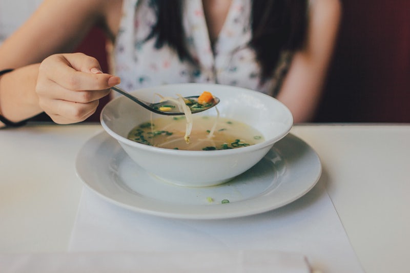 woman eating chicken noodle soup from white bowl