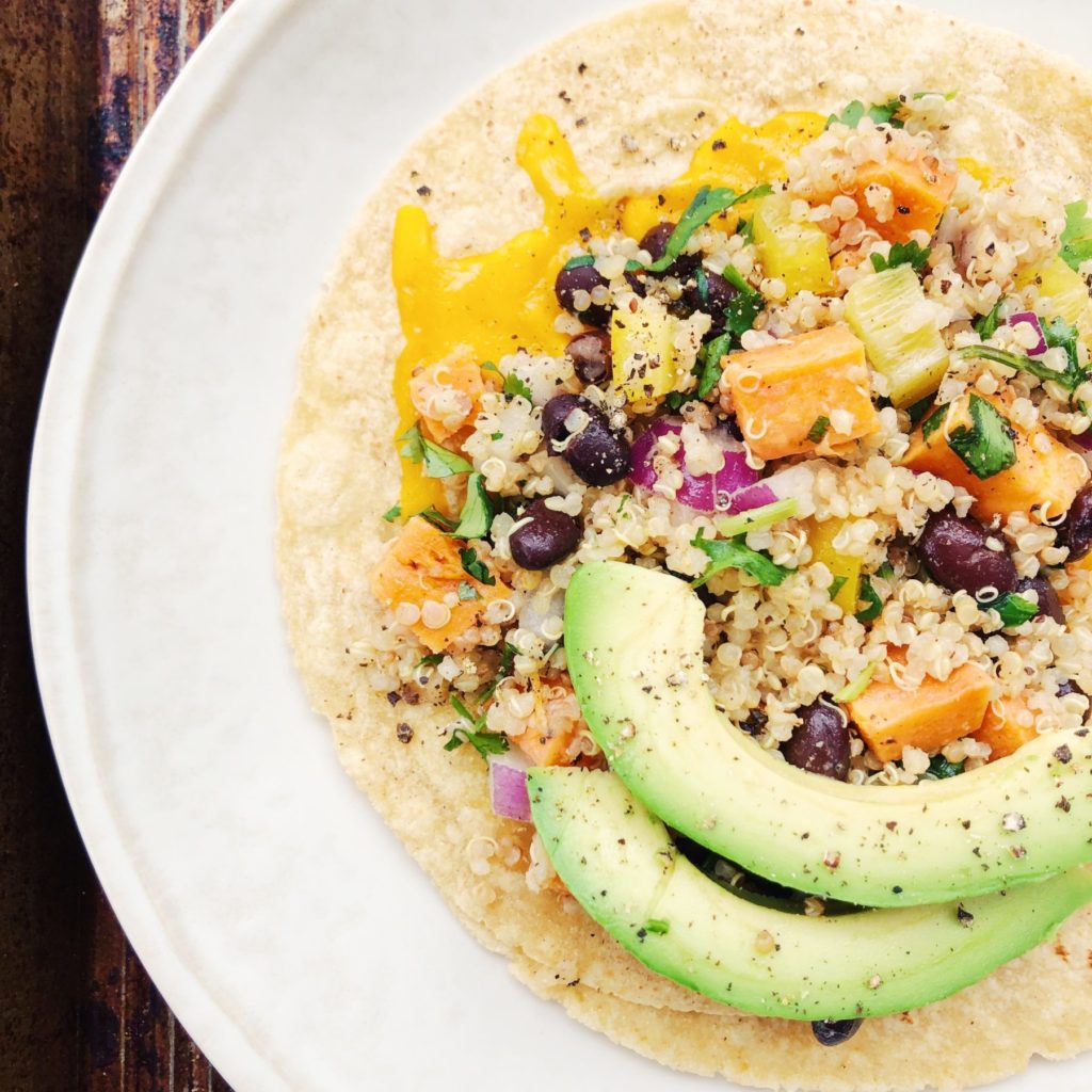 Taco with quinoa and black beans, cheese and avocado slices on a white plate