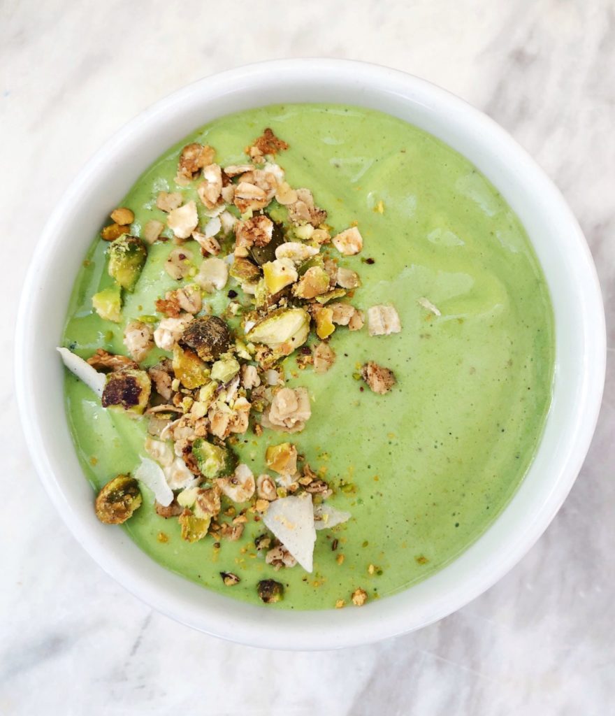 Overhead shot of green smoothie with granola on the left hand side placed in a white bowl