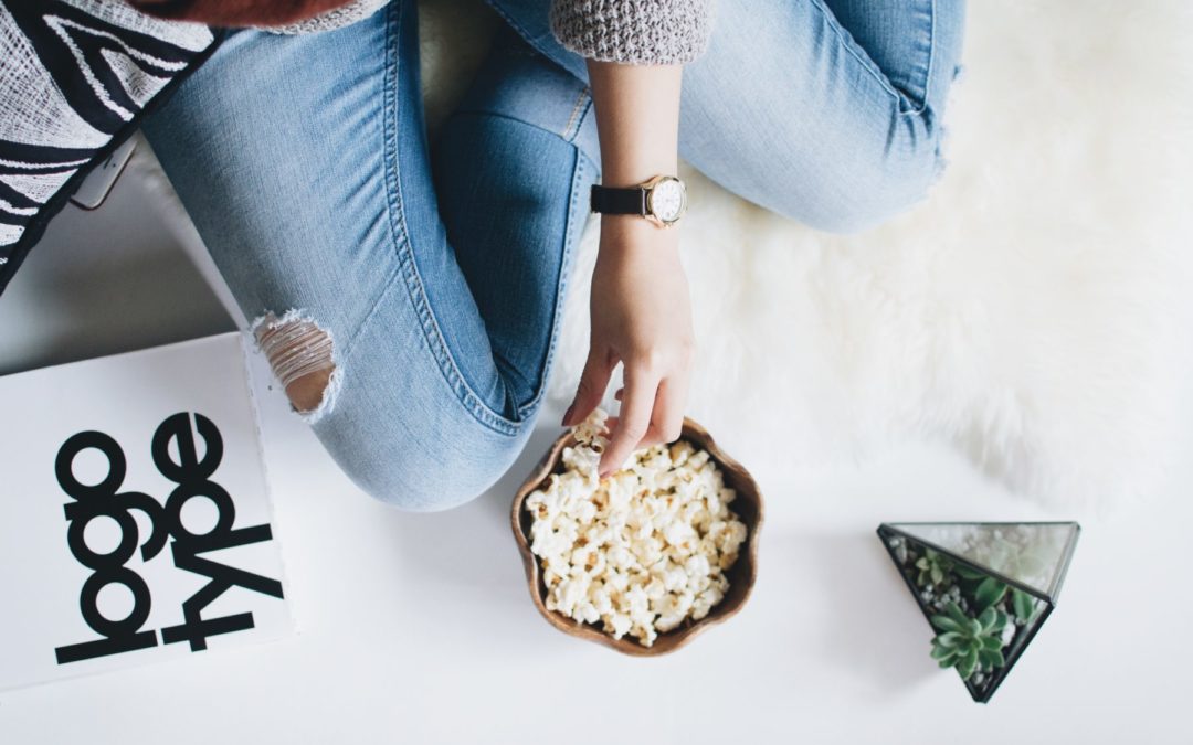 woman in jeans snacking on a small bowl of popcorn