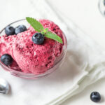 Bowl of pink berry ice cream with blueberries and mint in a clear bowl