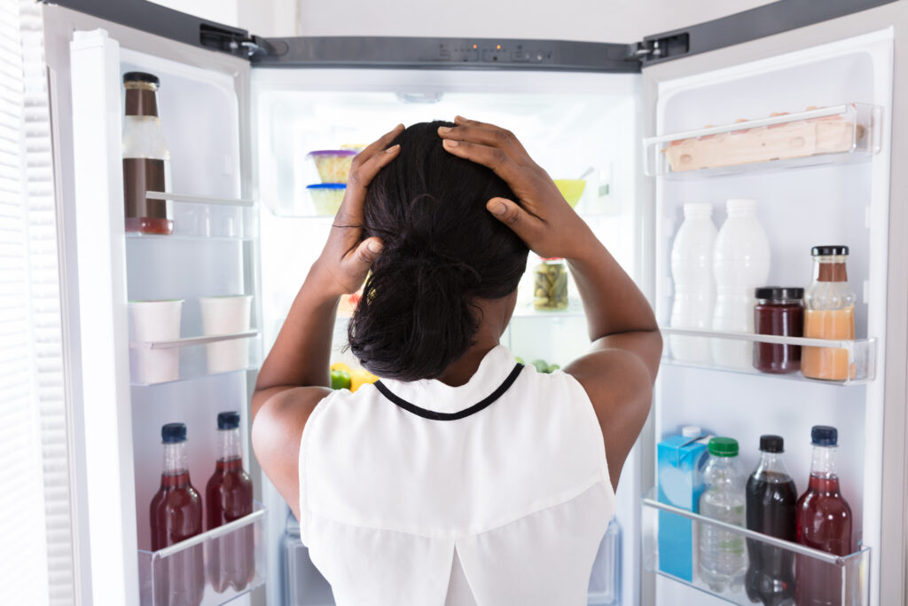 woman standing in front of an open refrigerator with her hands on her head in confusion