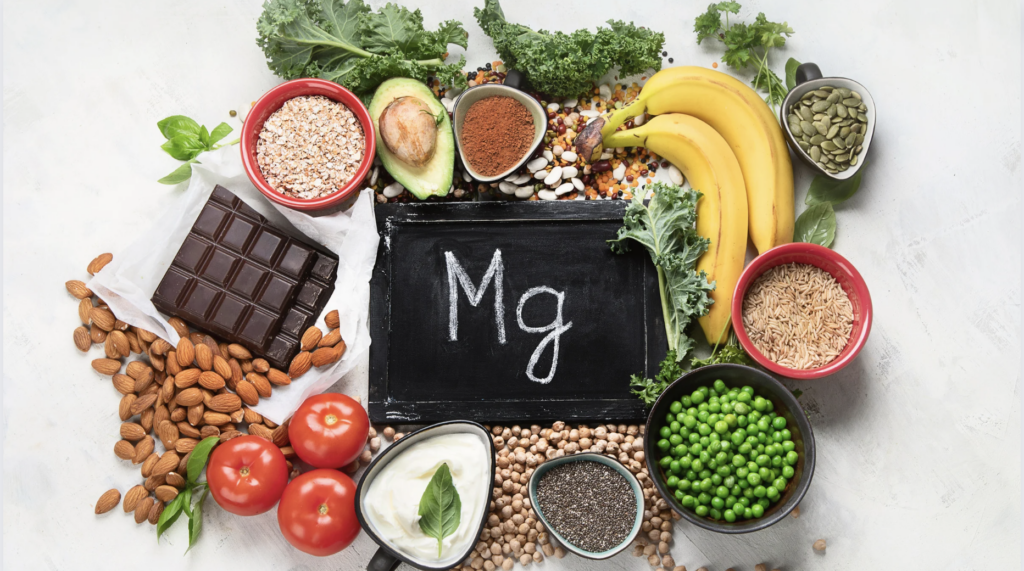 magnesium rich foods like pumpkin seeds, brown rice, peas, chia seeds, almonds and chocolate around a chalkboard that says MG