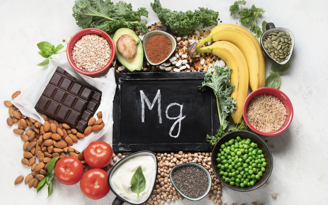 magnesium-rich foods such as almonds, dark chocolate, chia seeds, peas, bananas and pumpkin seeds surrounding a chalkboard with the words MG on it