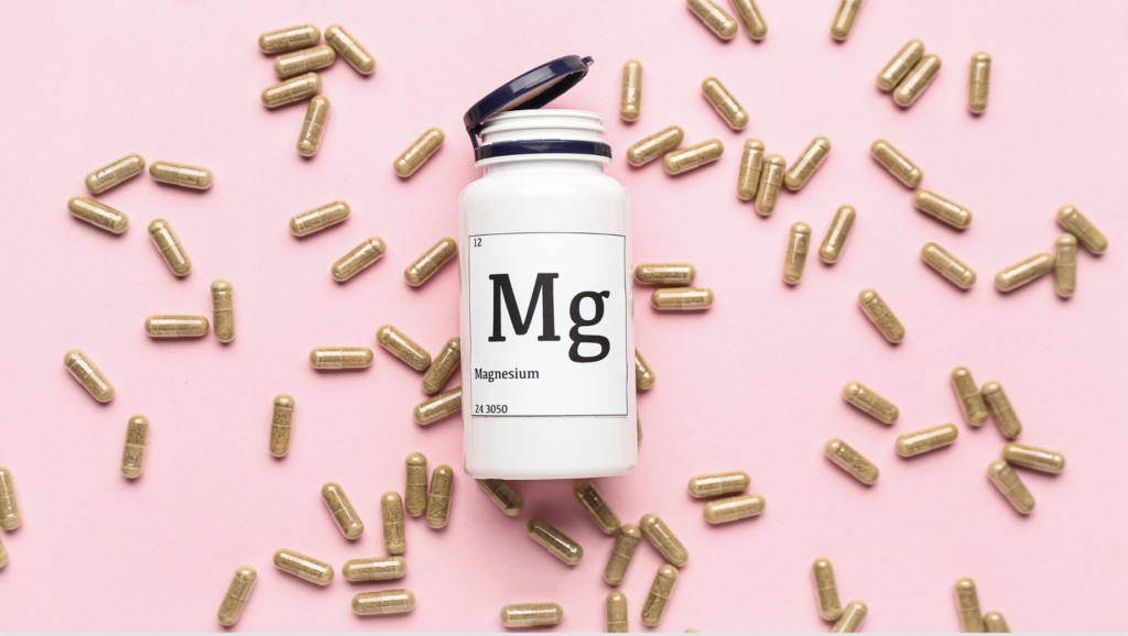 bottle of magnesium supplements with the pills outside the bottle on a pink background