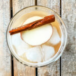 overhead shot of apple cider, apple, cinnamon stick and ice in a clear glass