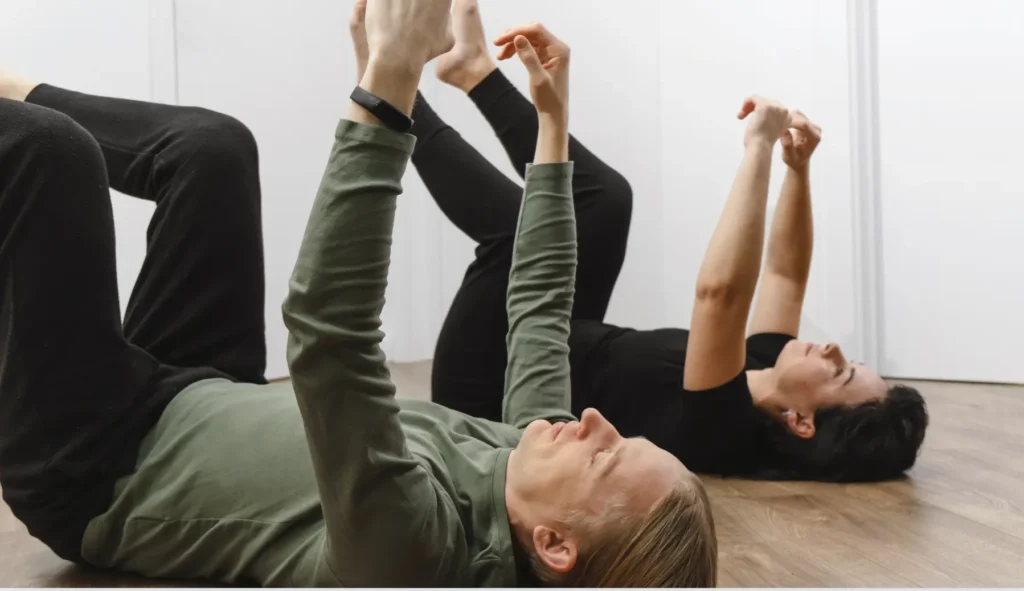 two people practicing Feldekrais on the floor with their arms up in the air