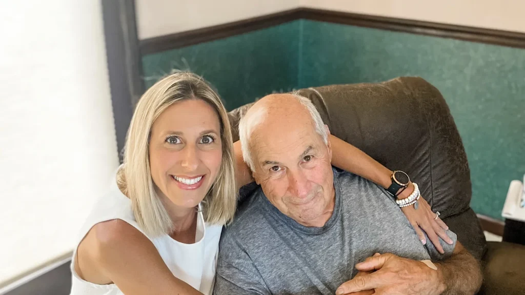 woman with her arms around an older man sitting in a brown recliner
